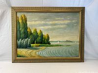 Full view of the framed oil painting depicting lakeshore with trees, water, sailboats, and sky