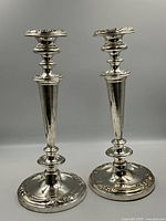 Front view of the pair of silver plated candle stick holders on a gray background