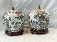 Front view of two lidded ginger jars on wooden stands showing painted floral and butterfly decoration
