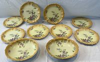 Ten antique porcelain berry bowls arranged on a white cloth. 8 smaller bowls and 2 larger oval bowls with scalloped edges and floral decoration.