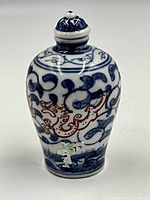 Front view of small Asian blue and white porcelain snuff bottle with floral and vine patterns, showing body detail with stopper in place.