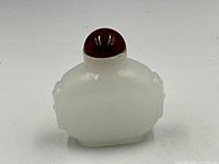 Small milk white jade snuff bottle with rounded edges and a deep red rounded cap, shown from front angle.