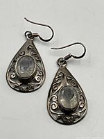 Close-up front view of earrings showing oval quartz crystals and ornate silver scrollwork.