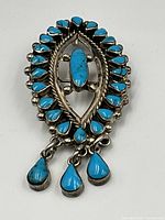 Front view showing turquoise stones set in silver brooch with three dangling turquoise drops.