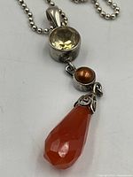 Close-up focused image of the pendant showing the faceted carnelian teardrop, small brown bead, and citrine-colored round stone with silver setting.