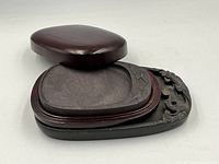 The stone inkstones laid out separately with the wooden case cover opened beside them showing their size and shape.