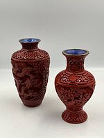 Front view of two cinnabar lacquer vases showing detailed carving and blue enamel lined rims