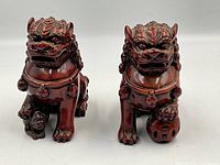 Front view of the two reddish-brown Foo Dog guardian statues showing facial features and posture.