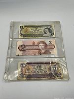 Three vintage Canadian bank notes including one, two, and ten dollar denominations in protective plastic sleeves