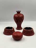 Full view of the four items: vase, lidded box, two ashtrays, showing carved details and brass/enamel accents