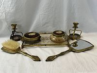 Full view of vanity set including brush, hand mirror, two lidded canisters on tray, and pair of candlestick holders arranged on white backdrop.