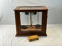 Front view of the fully assembled scale inside its wooden and glass case with the weights box displayed in front