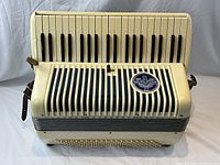 Front view of cream-colored Wurlitzer accordion showing piano keyboard, blue-striped metal grill and Wurlitzer logo