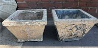 Pair of square cement planters side-by-side showing weathered surface and Fleur de Lis motif