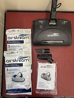 Photo showing three vacuum heads including one with beater bar, six new Air Stream vacuum bags, and owner's manual in plastic wrap.