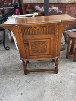 Front view of side cupboard showing carved front panel, single door, turned legs