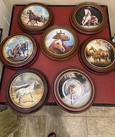 Top-down view of all seven collector horse-themed decorative plates arranged on the floor, showcasing variety of horse paintings in round wood frames.
