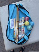 Top-down view of croquet set parts lying inside the open blue carrying bag on a white table outdoors.