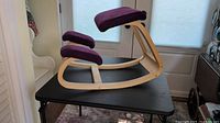 Side view of ergonomic kneeling rocking chair showing curved hardwood frame and purple cushions