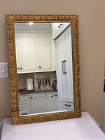 Full view of the rectangular mirror showing white kitchen cabinetry reflected and ornate gilded resin frame with leaf and scroll motifs.