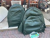 Six large and one small green plant tents outdoors, showing dome shape and zippered fronts
