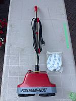 Full view of the Pullman-Holt floor polisher, showing handle, power cord wound on handle, device body, and polishing pad in original packaging.
