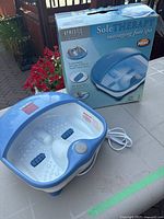 Blue and white electric foot spa placed on a table, alongside the original packaging box featuring product branding and images.
