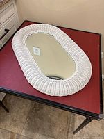 Top-down view of the oval white wicker mirror lying flat on a table with red surface.