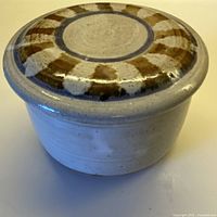 side view of lidded jar showing cream speckled body and decorated lid