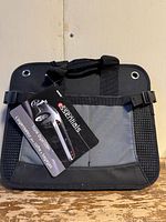 Front view of the black and gray Automotive Essentials collapsible car trunk organizer with attached branded hang tag