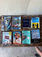 Top-down view of eight books placed on a wooden surface against a light wall, showing covers of all books clearly.