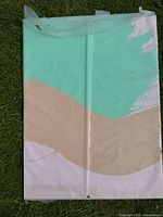Front view of the minimalist original acrylic painting showing three large blocks of color: mint green, beige, and off-white. The painting is protected by a clear plastic covering and lying on grass.