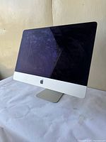 Front left angle view showing the iMac with the screen off, aluminum body, and part of the crack in the top left corner.