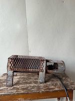 Side view of the industrial Salamander propane heater showing mesh guard and cylindrical heating tube on a metal table against a plain wall.