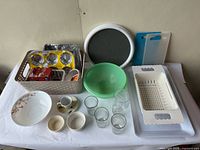 Overview of assorted kitchenware items including bowls, mugs, glasses, trays, cutting boards, and a colander.
