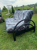 Side angle of futon showing curved black metal armrest and mattress with abstract patterned cover.