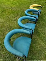 Four cantilever dining chairs on grass showing curved tubular black steel frames with worn blue-green pleather upholstery; one chair is yellow and damaged on armrest.