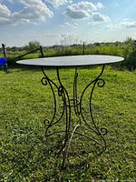 Full view of round steel table standing on grass with clear sky background, showing table top and leg design.