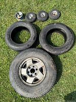 Photo showing two large Firestone Winterforce truck tires, one mounted on a solid cast 6 bolt rim, and four small utility tires with metal rims