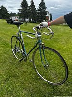 Side and front angle showing turquoise steel frame, white wrapped drop handlebars, black saddle, and front wheel details