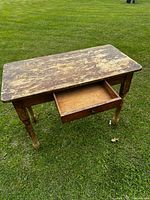 Top view of vintage wooden writing table showing worn, chipped surface and open drawer with built-in organizer compartment