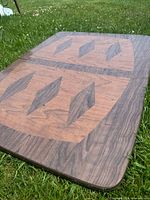 Top view of vinyl woodgrain tabletop showing geometric leaf-shaped patterns with visible scuffs on surface.