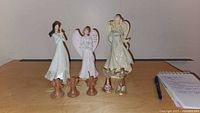 Photo showing three standing angel figurines and five smaller hanging angels on a table.