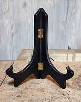 Front view of a black wooden book or plate easel showing two hinged panels and curved support legs.
