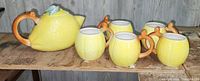 Full set of lemon-shaped ceramic teapot and five matching mugs displayed on a wooden surface.