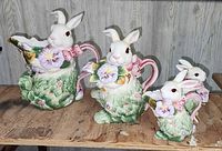 Front view of the full lot showing all four ceramic rabbit pieces including tea pot, pitcher, creamer and sugar container with floral designs and pink bows.