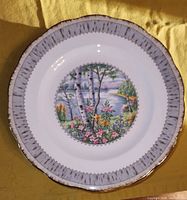 Close-up of one Royal Albert Silver Birch pattern dinner plate showing design detail of silver birch trees by a lakeside with flowers and gold-trimmed edge.