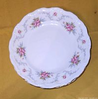Top view of a single Royal Albert Tranquility china dinner plate showing pink rose floral clusters, gray scrolling patterns, and gold trim on scalloped edge.