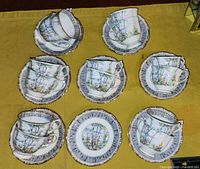 Photo showing an arrangement of 14 Royal Albert Silver Birch tea cups paired with 17 matching saucers on a yellow surface.