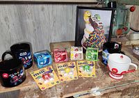 Photo of 12-piece M&M's collectible lot including mugs, USB flash drives, candles, and framed picture.